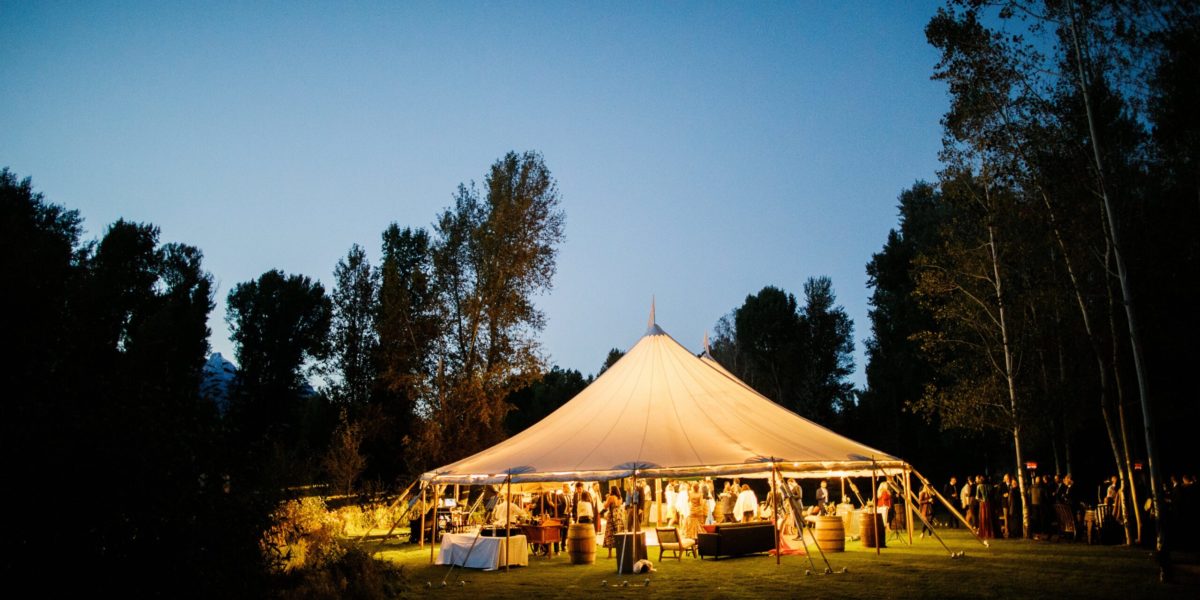 event_tent_at_night A large tent full of guests is lit up at night while surrounded by trees