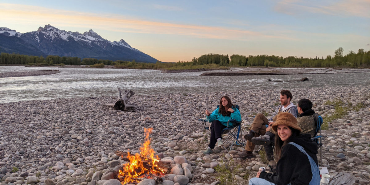 bonfire_river A group of friends sit around a sunset bonfire next to the river and mountains